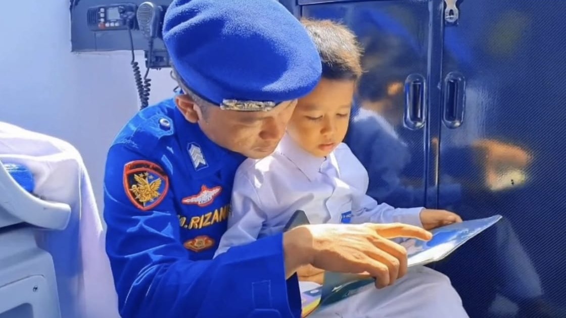 Salah satu anak TK Khadijatul Kubra Mantuil dipangku personel Sat Polairud Polresta Banjarmasin sembari membaca buku di dalam Perpustakaan Terapung, Kamis (23/1/2025). Foto: Humas Polresta Banjarmasin